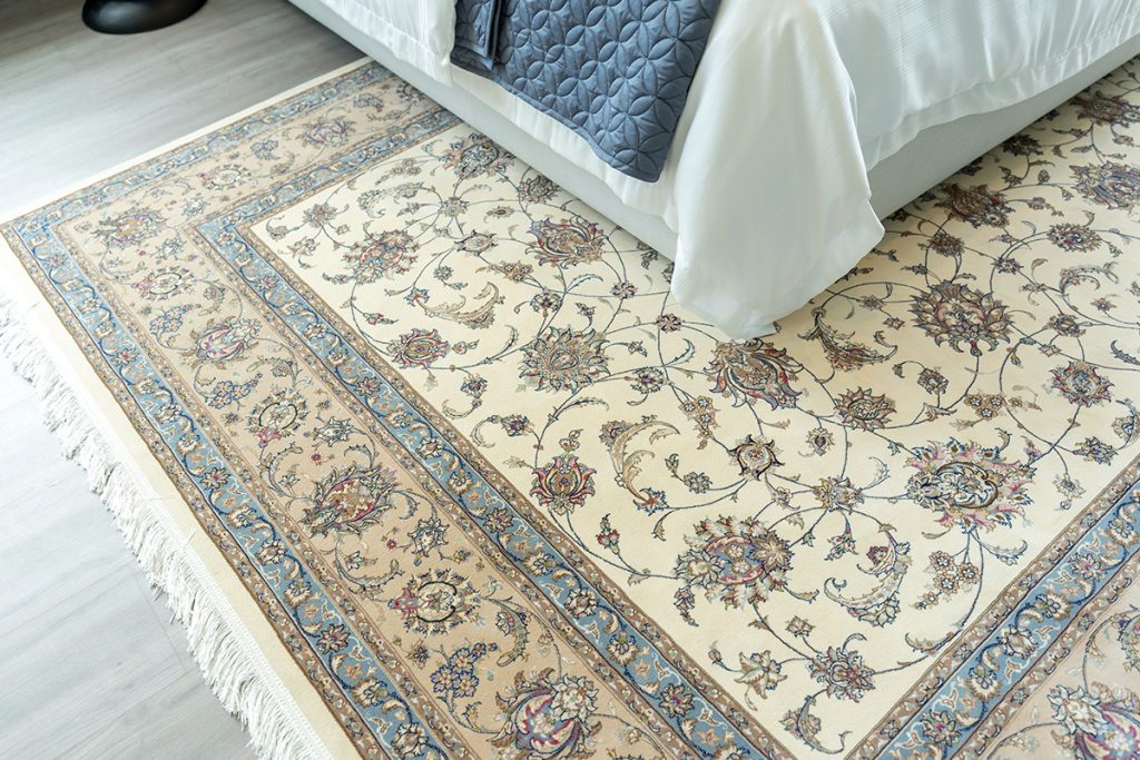 A cream and blue oriental rug beneath a bed to illustrate David Tiftickjian And Son's professional rug cleaning services.