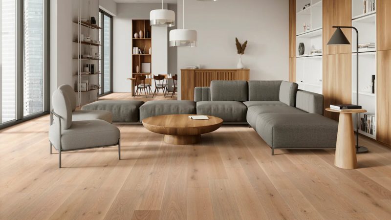 A bright living room with a gray couch and wide-plank wood floor – a 2026 floor trend.