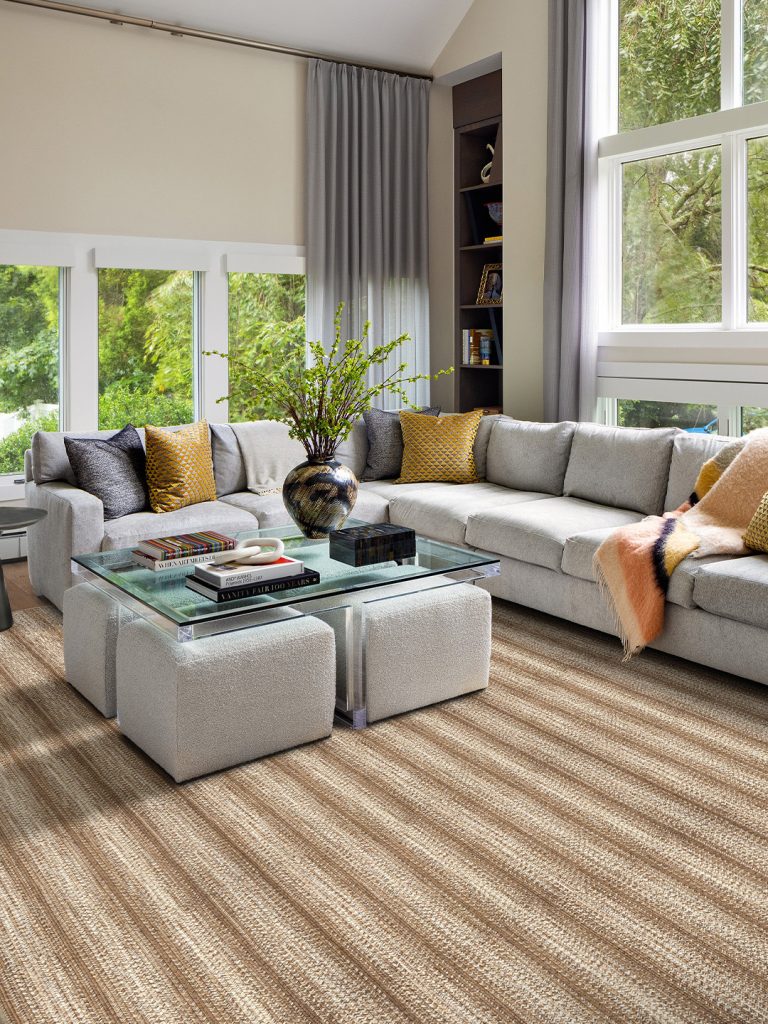 A brown striped rug with a white couch and ottoman.