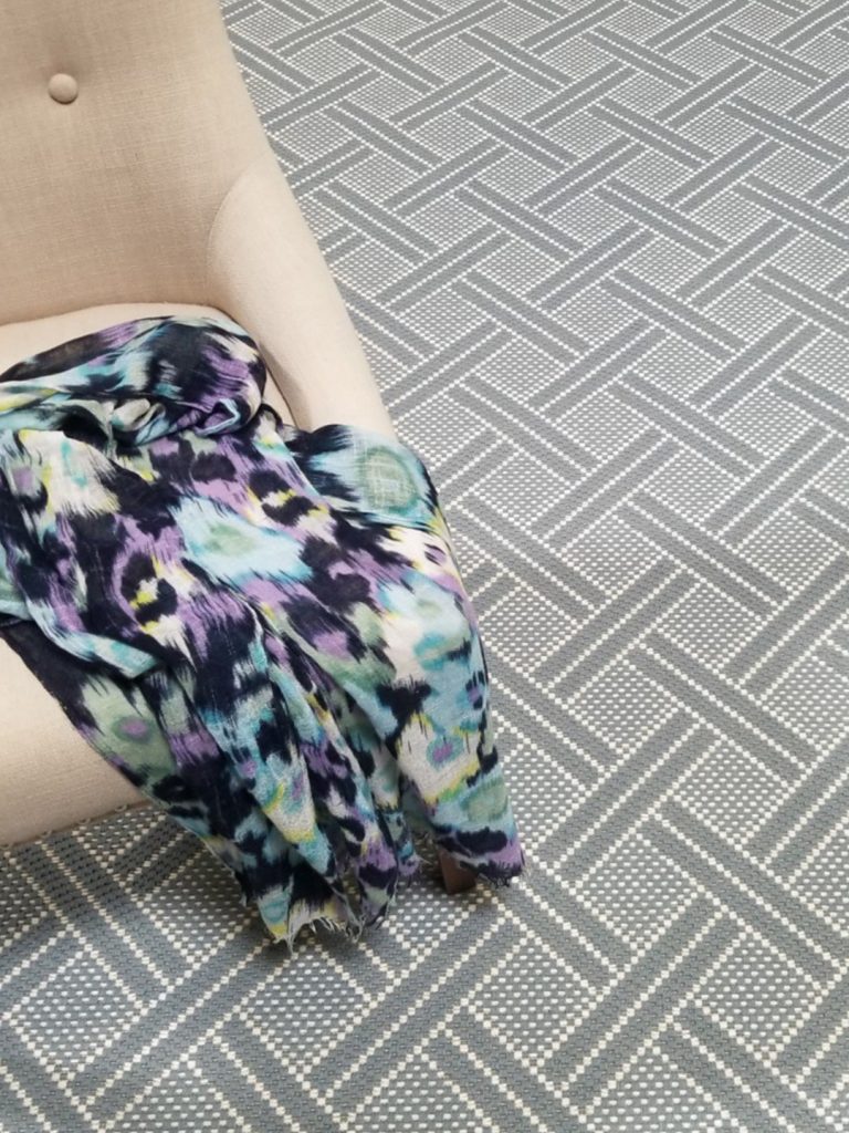 A blue patterned rug with a beige chair and multicolored scarf.