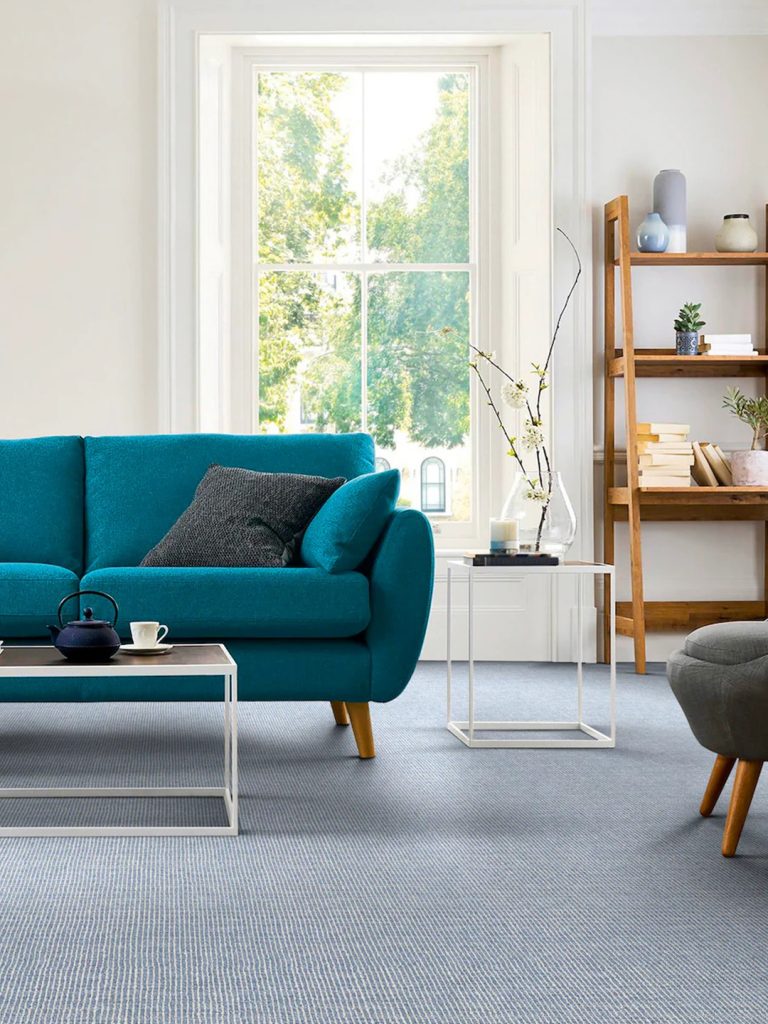 Blue patterned carpet beneath a teal sofa with wood shelves and a window in the background.