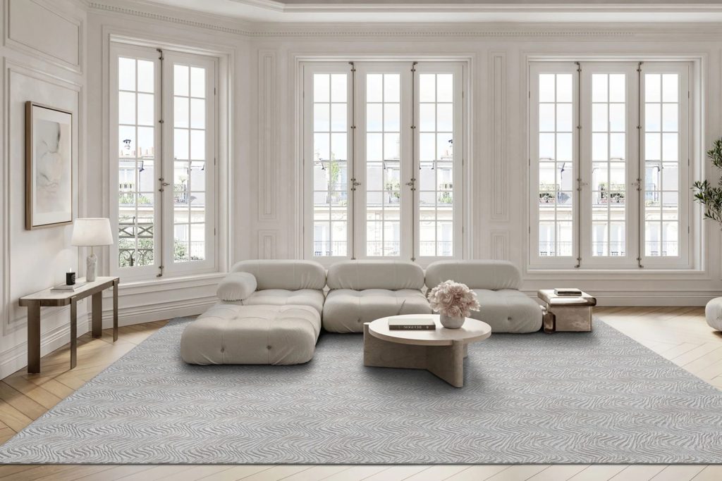 A gray carpet cut to size in front of large windows with a neutral colored sofa.