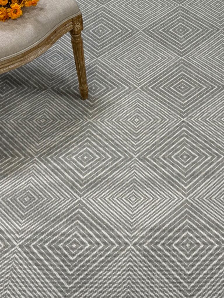 An gray square patterned carpet with the corner of a chair for our spring carpet inspo.