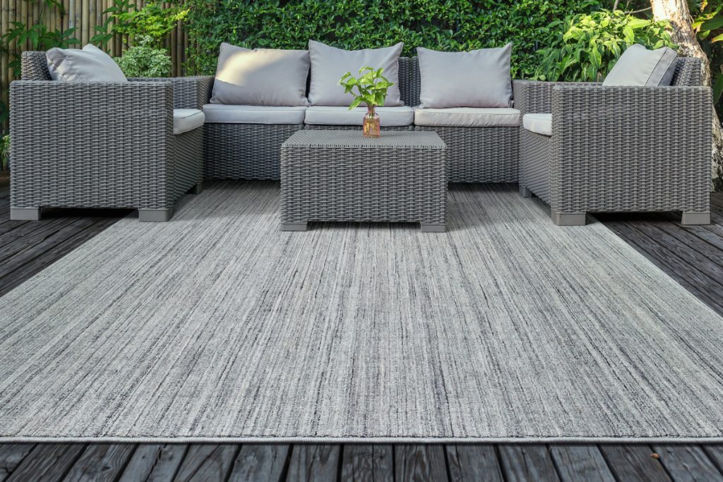 A gray textured outdoor rug on a gray wood patio with gray patio furniture and a green ivy colored wall in the background.