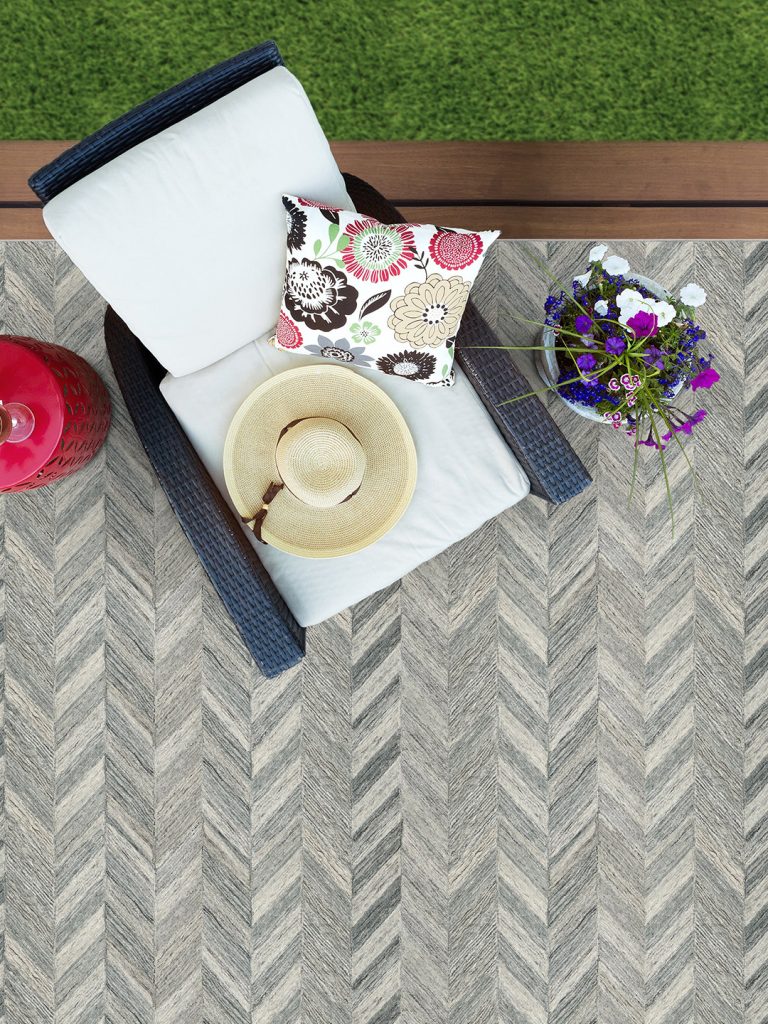 A gray herringbone patterned outdoor rug with flowers and a white and blue patio chair.