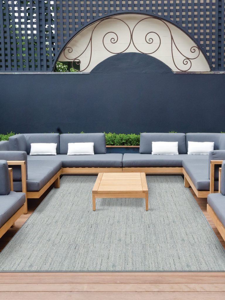 A light blue textured outdoor rug with blue patio furniture and a blue wall in the background.