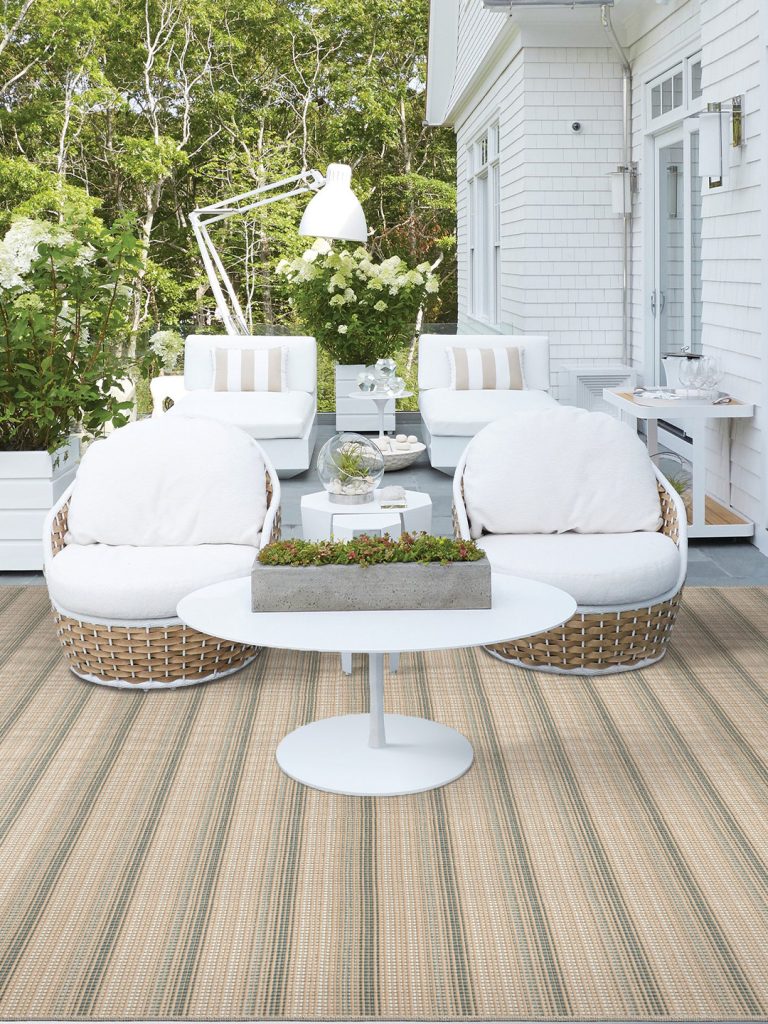 A beige and green striped outdoor rug on a gray tile patio with white patio furniture.