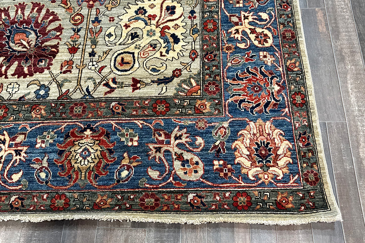 Corner of a veggie dyed rug with a gray base featuring multiple colors and a traditional design against a gray wood floor.