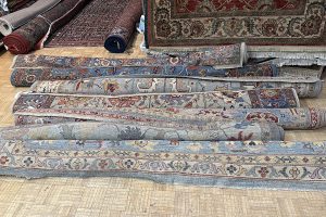 Rolled up oriental rugs in a pile waiting for professional rug cleaning service. | Freshly cleaned rug promotion.