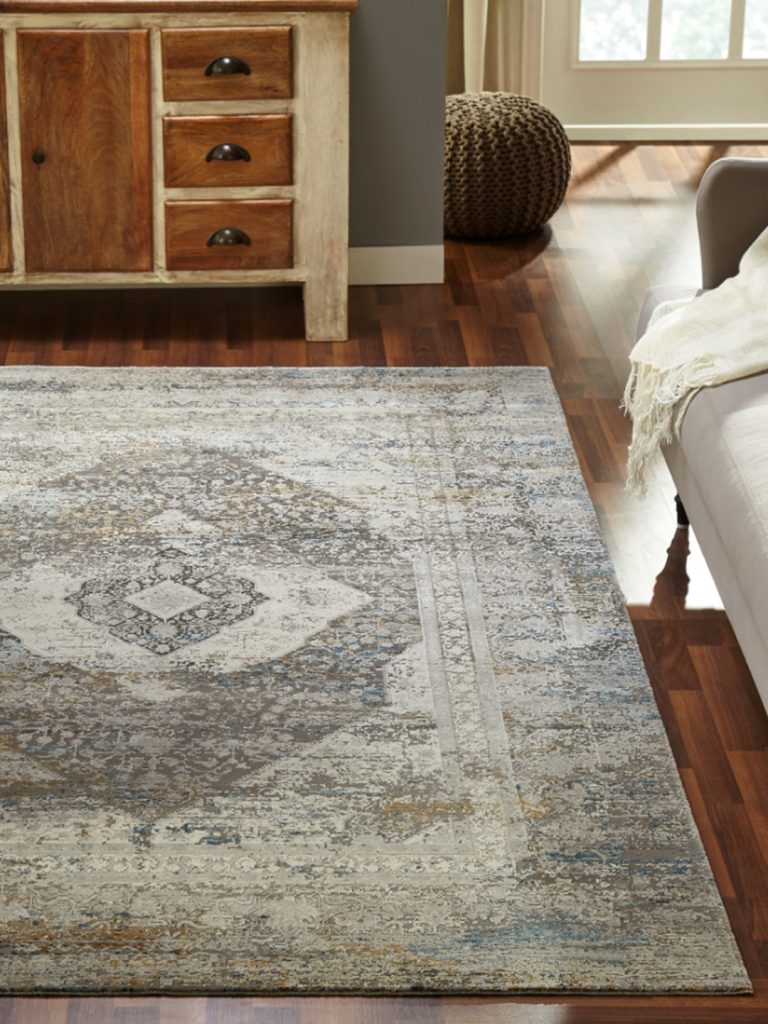 A machine-made oriental rug with a large central medallion in neutral tones in a living room setting.