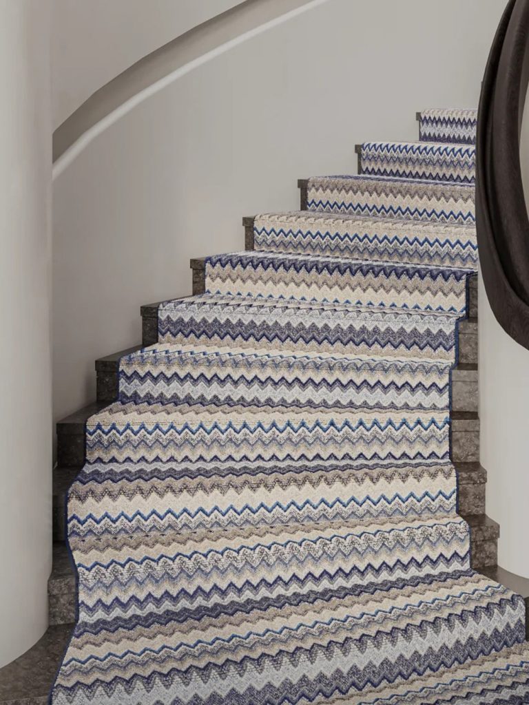 A blue, white, and brown wave-patterned residential carpet going up a curved staircase.