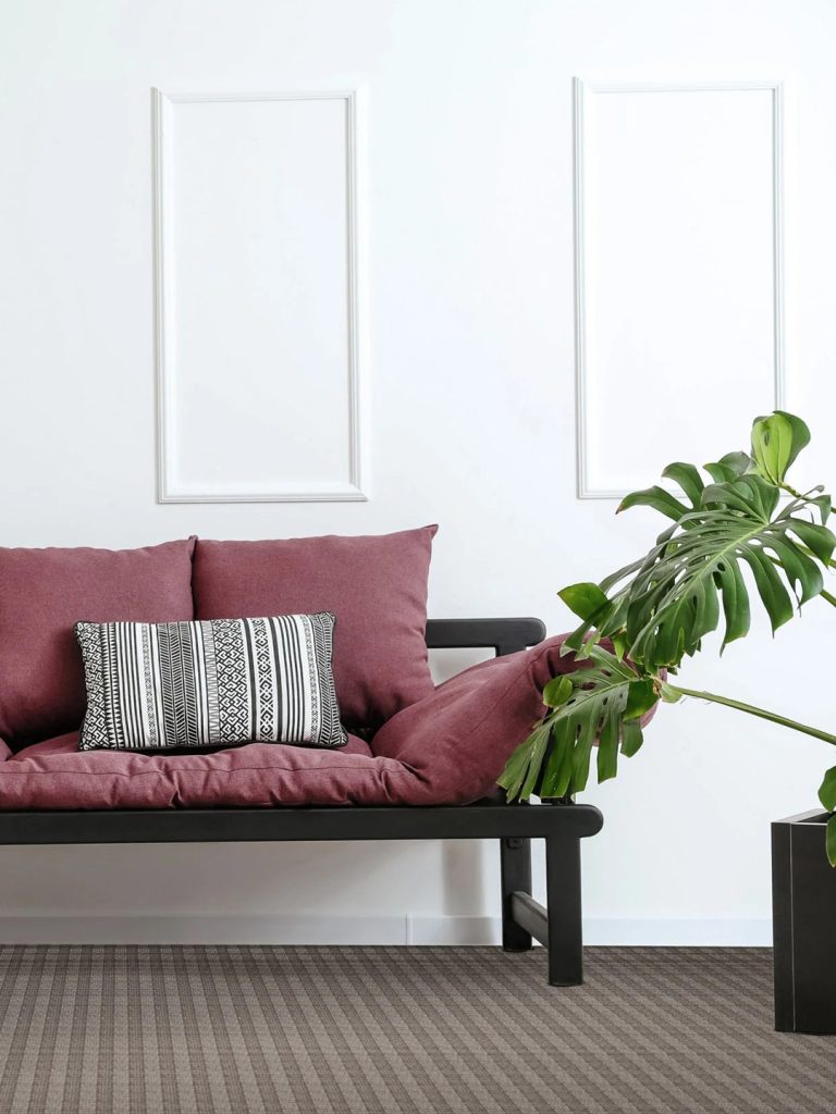 A dark brown striped residential carpet beneath a dark bench with dark red cushions beside a potted plant.