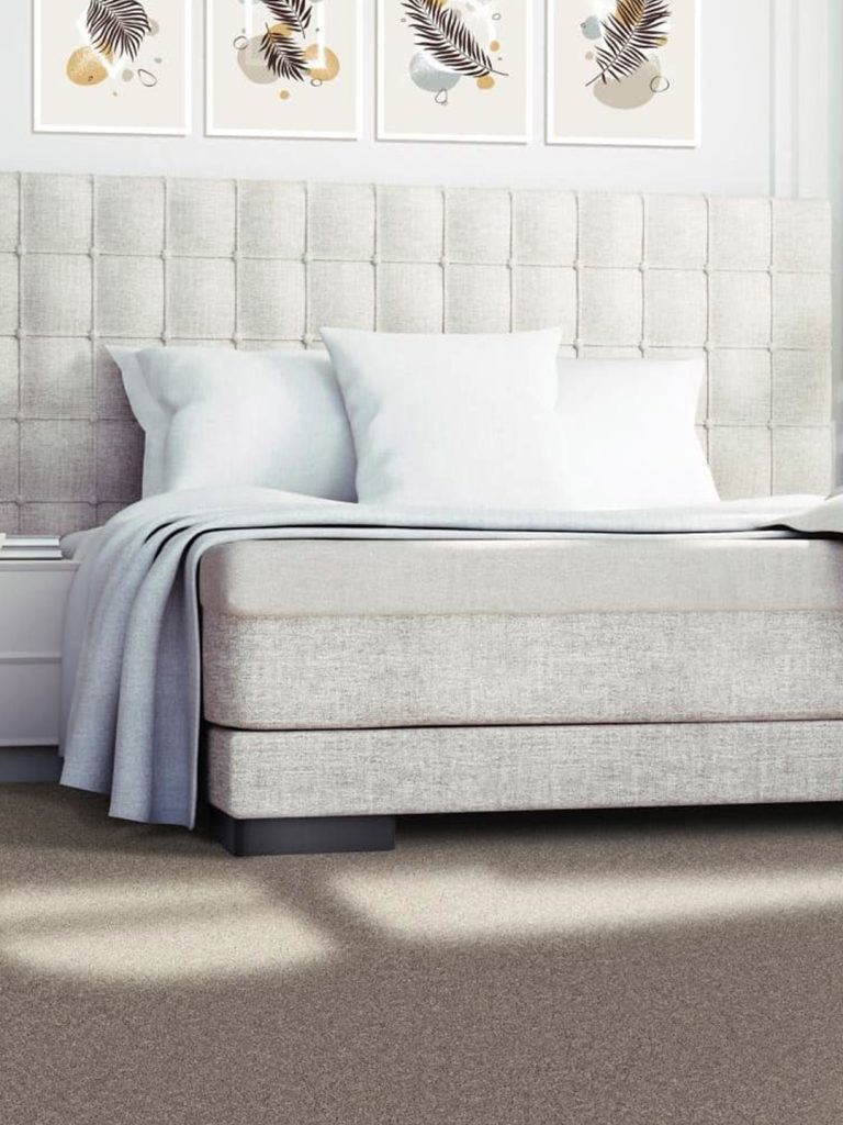 Brown residential carpet beneath a gray and white bed.