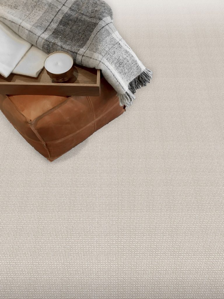 A light brown patterned residential carpet beneath a leather chair with a gray blanket.