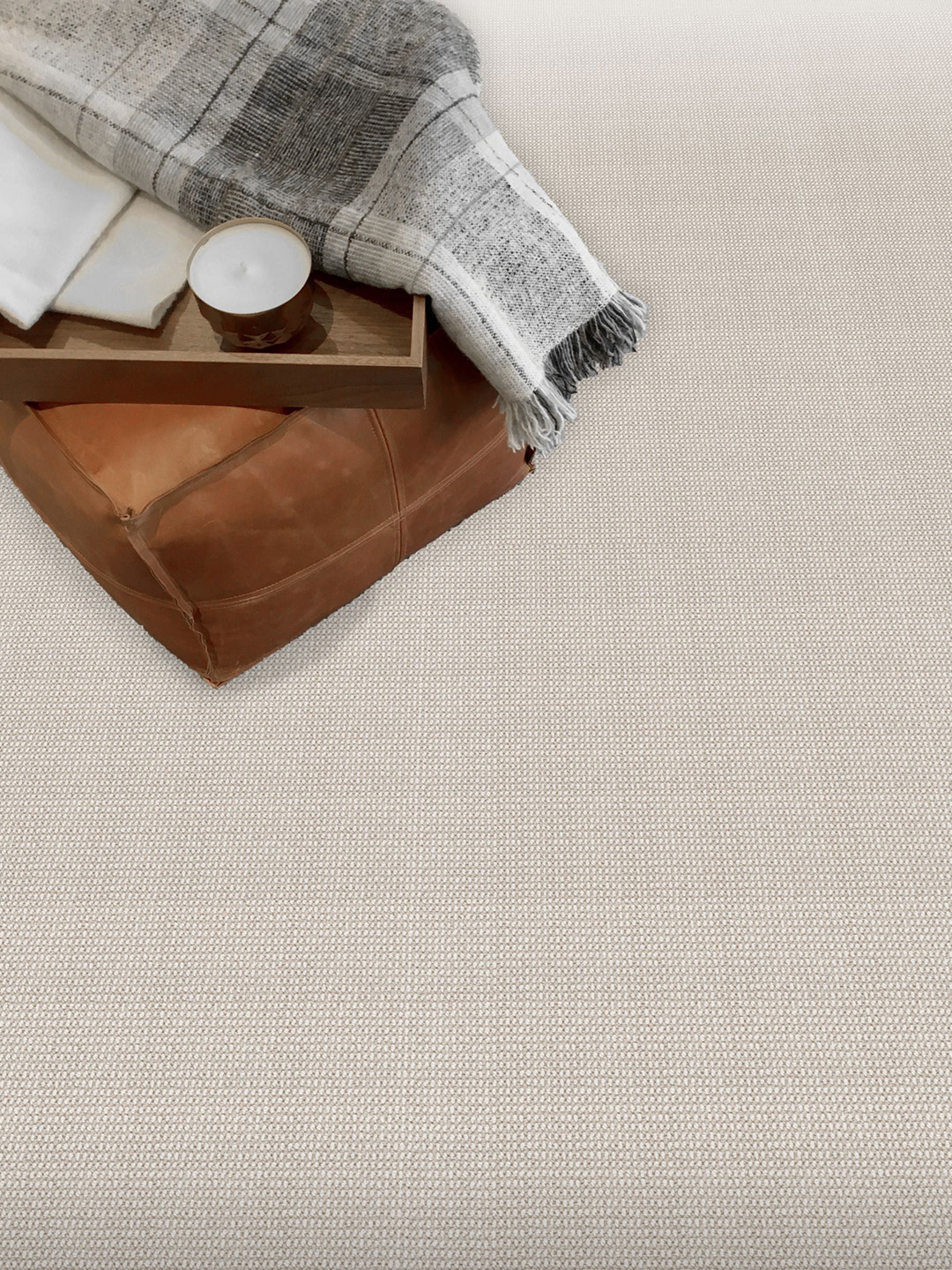 A light brown patterned residential carpet beneath a leather chair with a gray blanket.