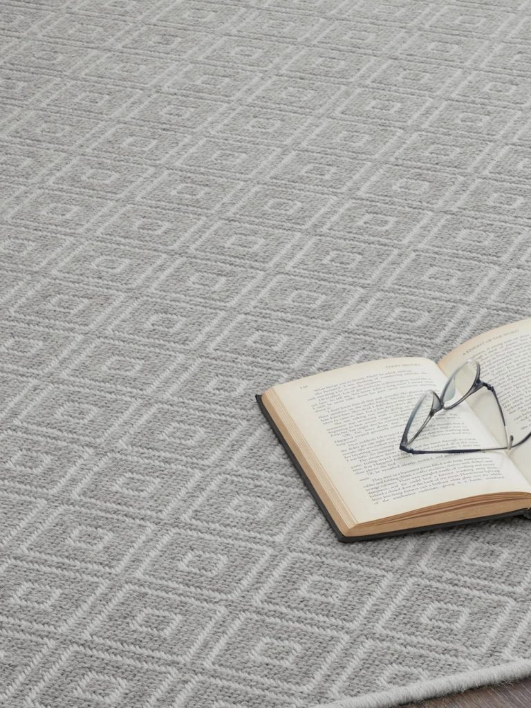 A gray geometric patterned residential carpet with an open book and glasses on top.