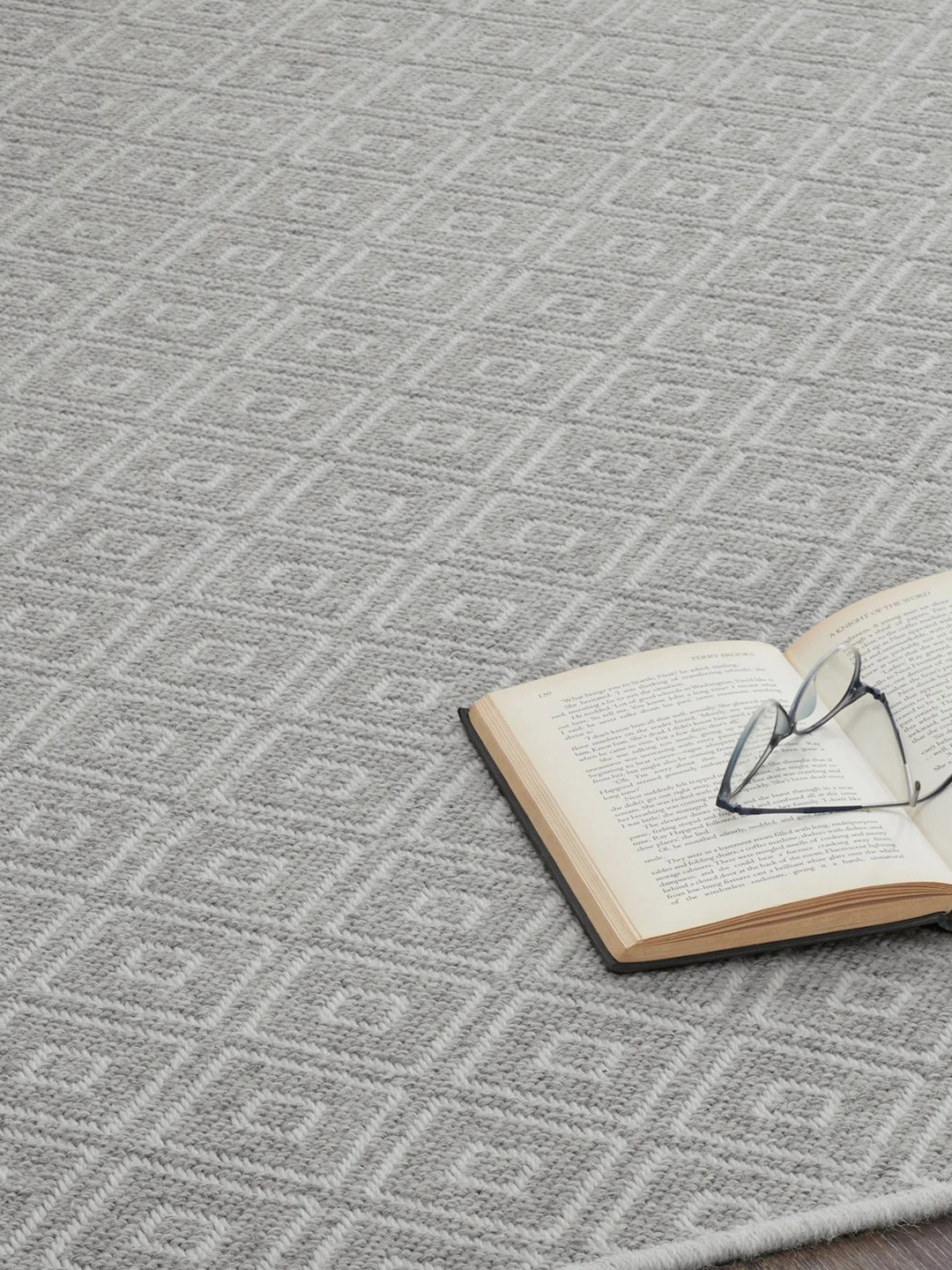 A gray geometric patterned residential carpet with an open book and glasses on top.