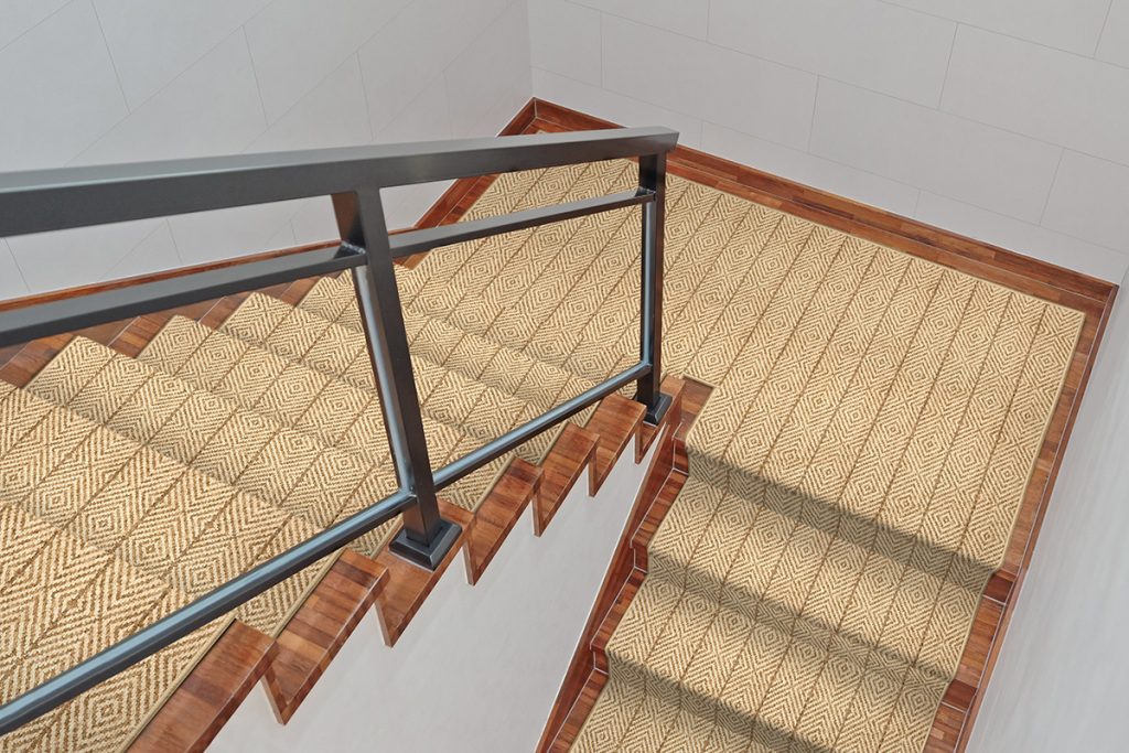 A beige stair runner rug with a subtle geometric pattern and an iron handrail.