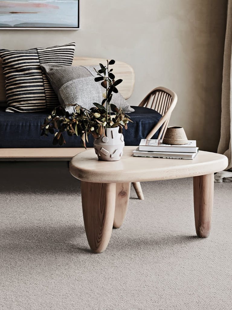 Neutral colored wool carpet with a triangle wood coffee table and dark sofa.