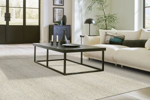 A light colored wool carpet under a grey coffee table and white sofa.