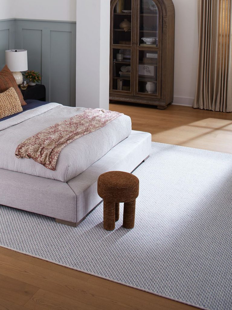 A grey and blue patterned wood carpet on a hardwood floor with a grey bed and foot stool.