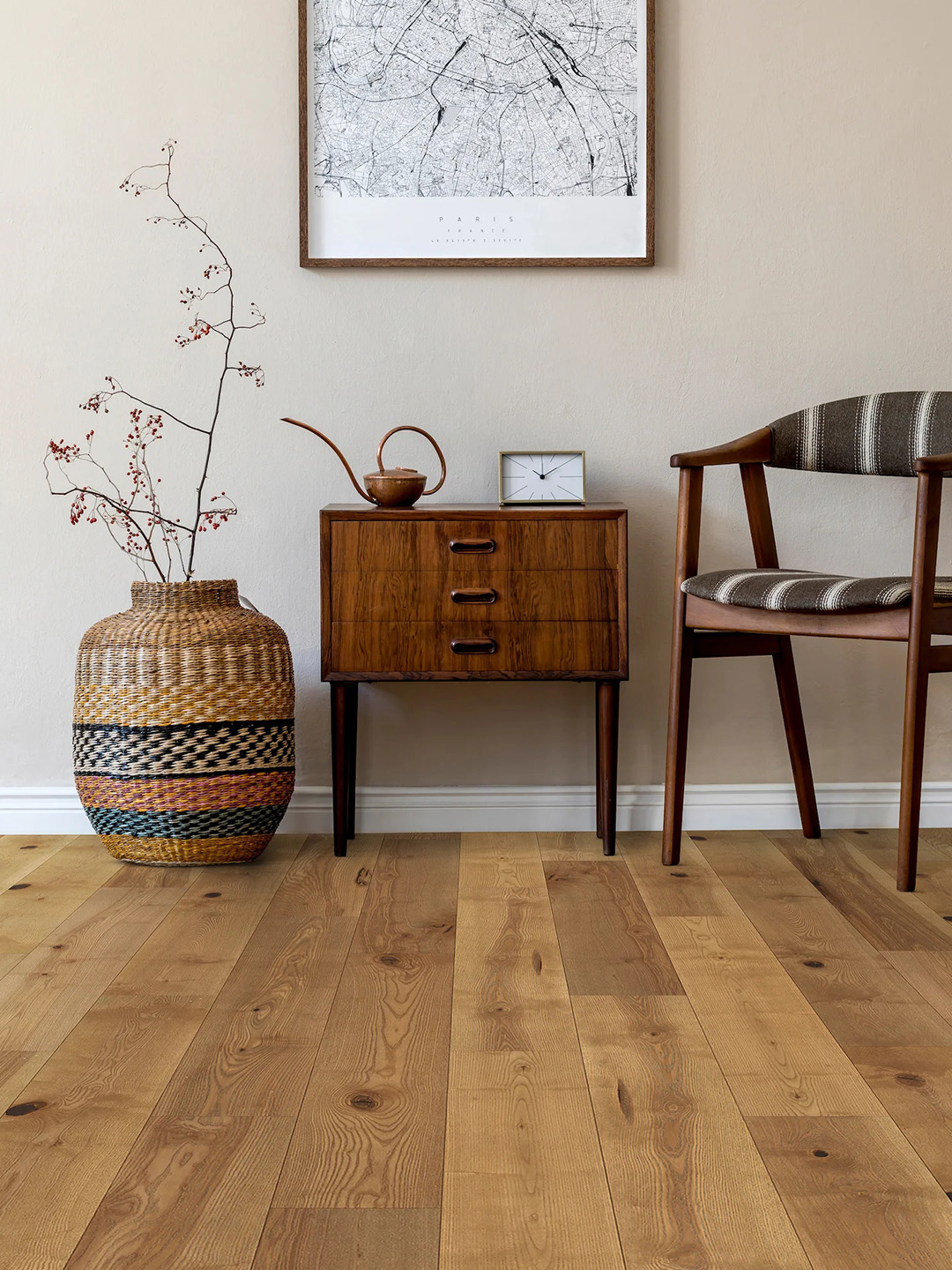 Shades of natural hardwood flooring with a vase, chair, and end table against a light colored wall.
