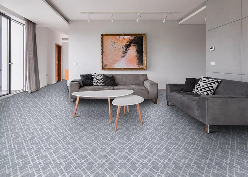 A gray and white geometric broadloom carpet in a living room setting with gray furniture and a large abstract painting on the wall.