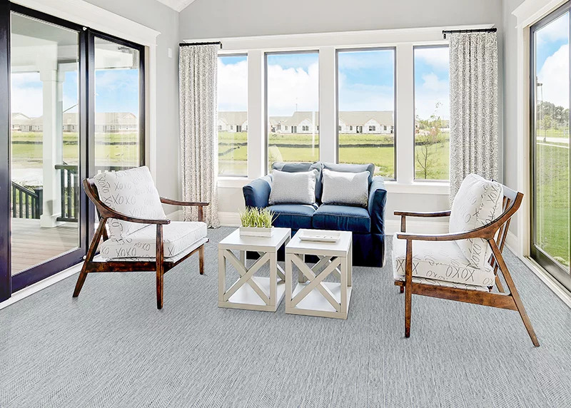 A gray textured broadloom carpet in a sunroom with white chairs and a blue couch.