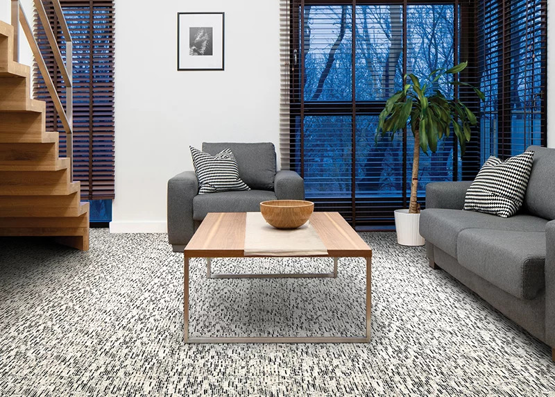 A gray and blad textured broadloom carpet with gray furniture and a wood coffee table.