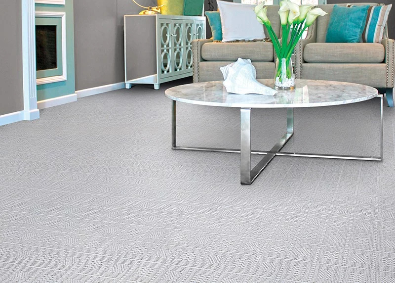 A gray textured broadloom carpet in a living room setting with gray furniture and teal accents.