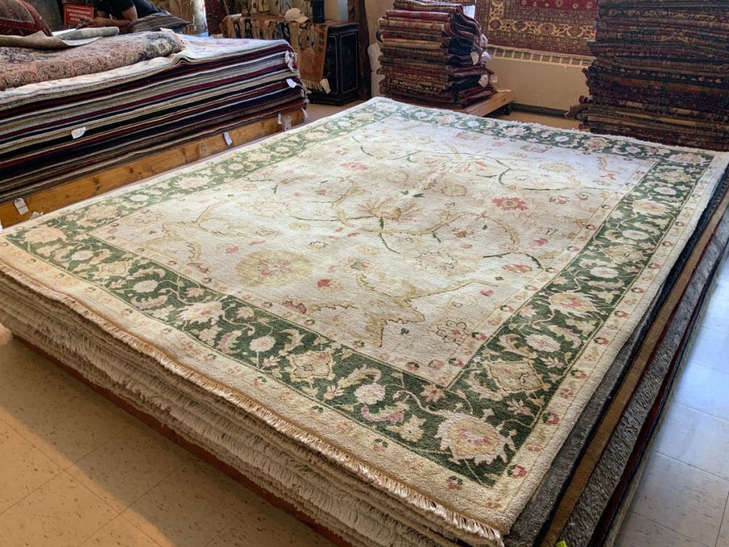 A cream colored vintage rug with a green border and a soft oriental design.